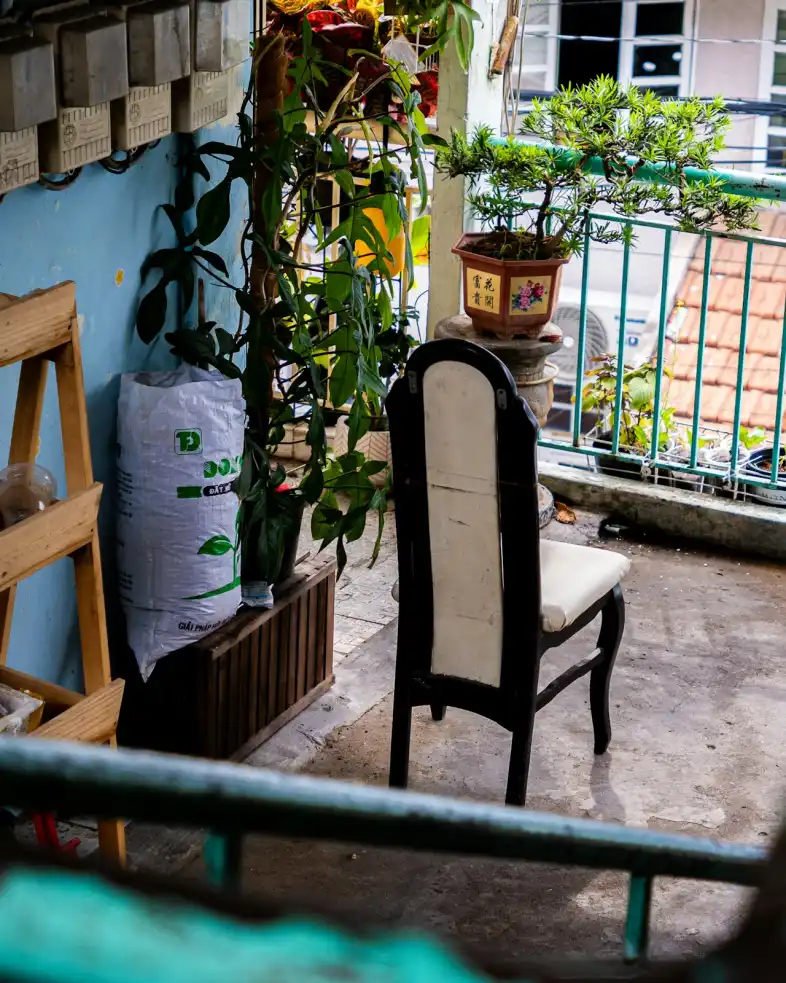 Phòng loft có ban công: ban công nhỏ nhiều cây xanh, ghế gỗ tựa lưng và chậu cây, phía xa là mái nhà